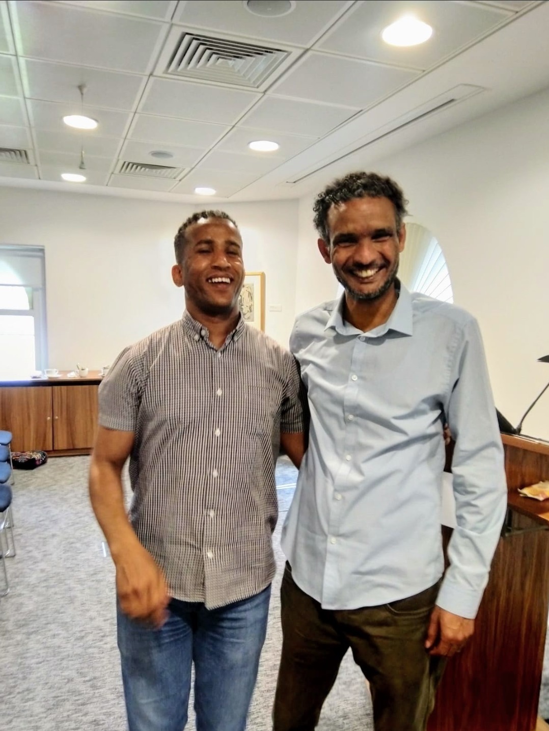 Photo of 2 men standing together and smiling in an office.