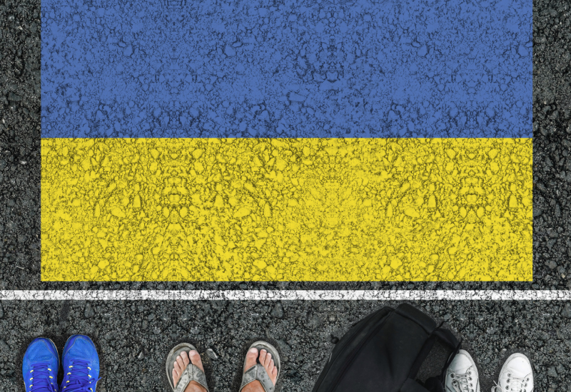 People's legs standing on asphalt road on which the flag of Ukraine is drawn.