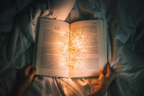 Photo of a person holding string lights on an opened book.